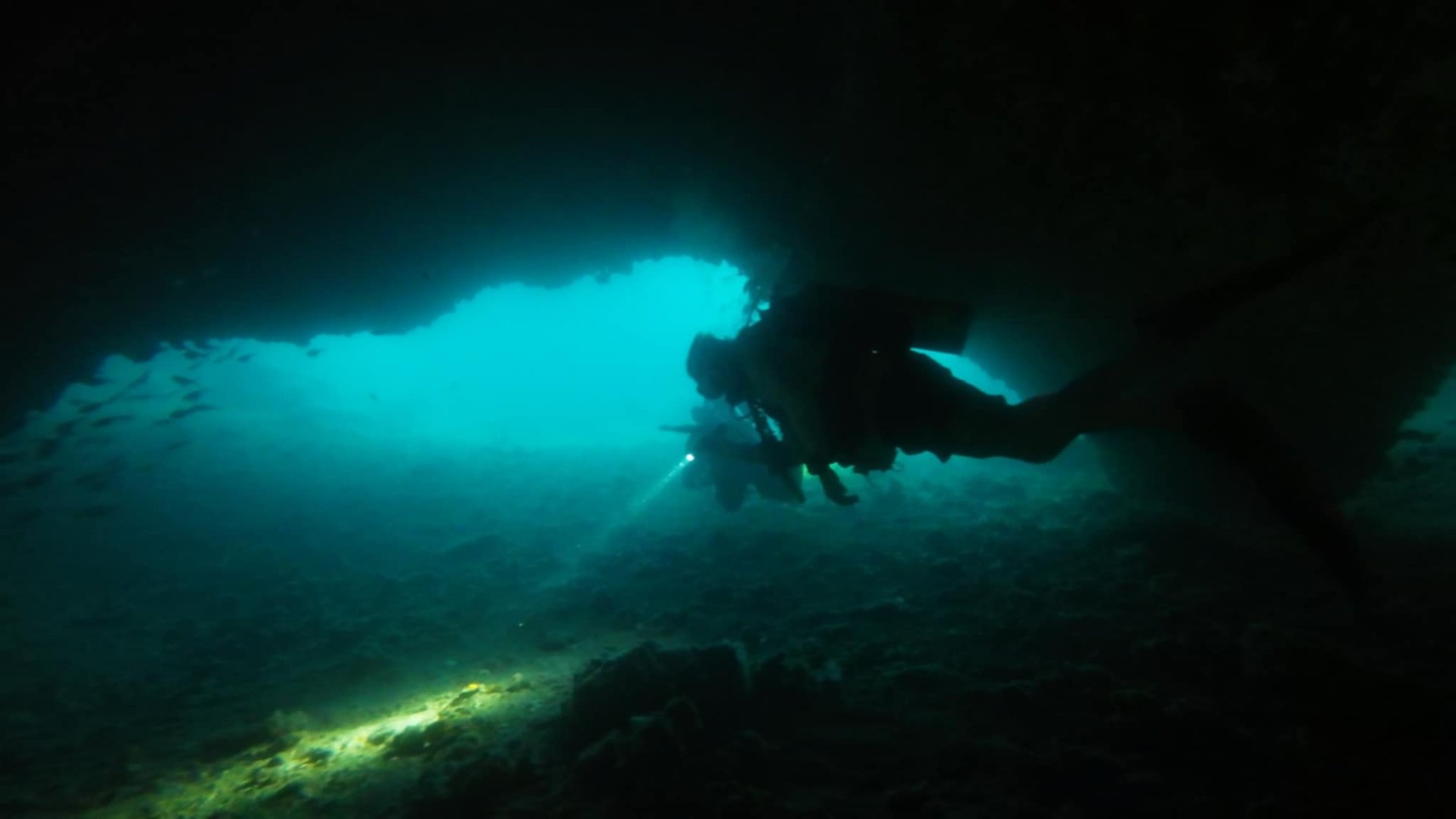 Scuba diver exploring underwater cave with bright blue light filtering from opening above