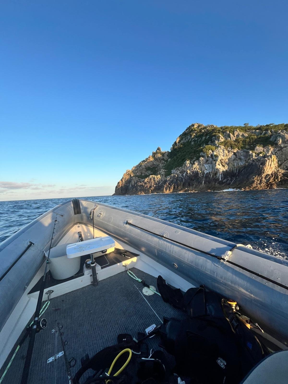 View from a boat heading toward a rocky coastal cliff under clear blue sky and calm sea water