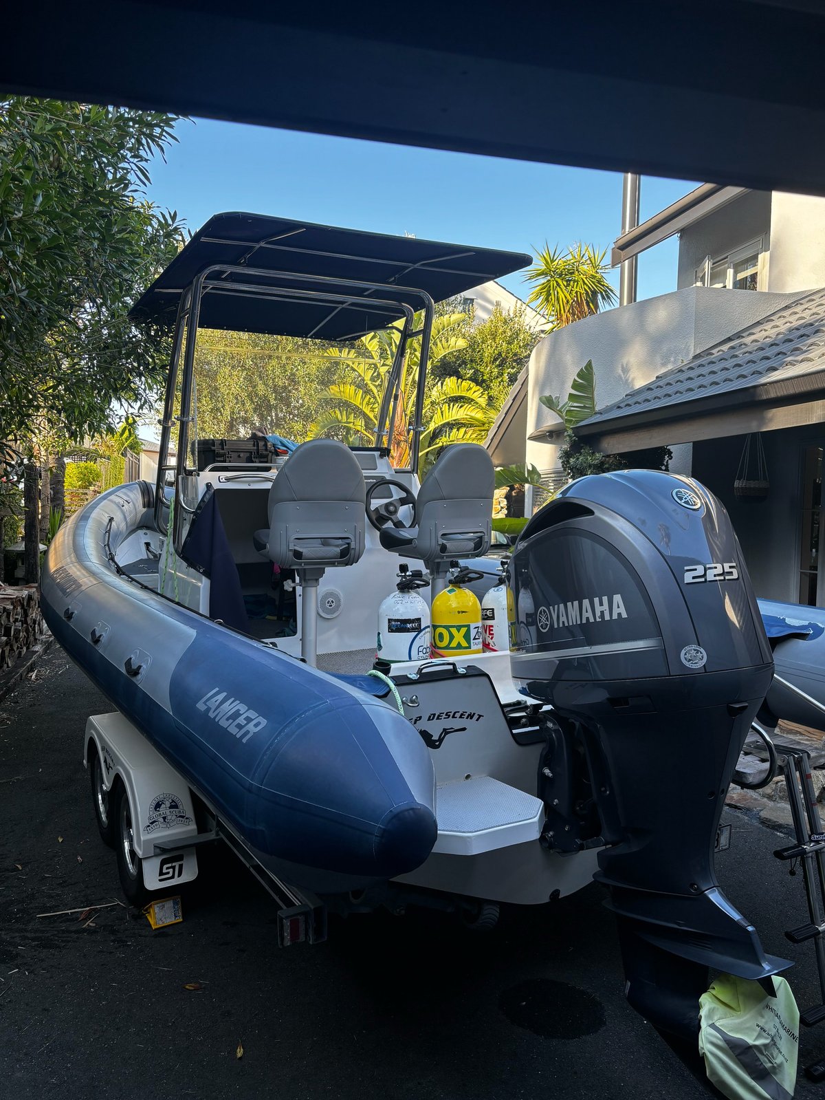 Blue and white inflatable speedboat with Yamaha 225 outboard motor parked on a trailer in a driveway