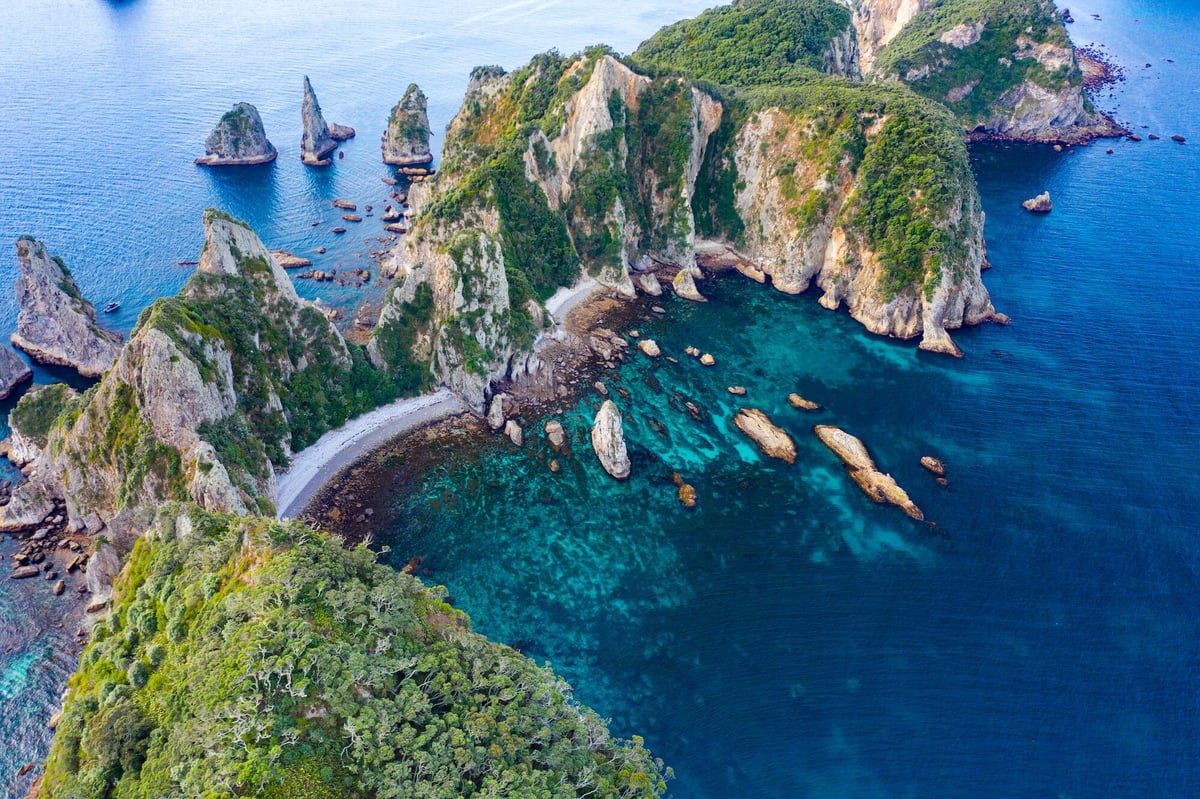 Aerial view of dramatic rocky cliffs and lush green vegetation surrounding a turquoise bay with boats, tropical island landscape