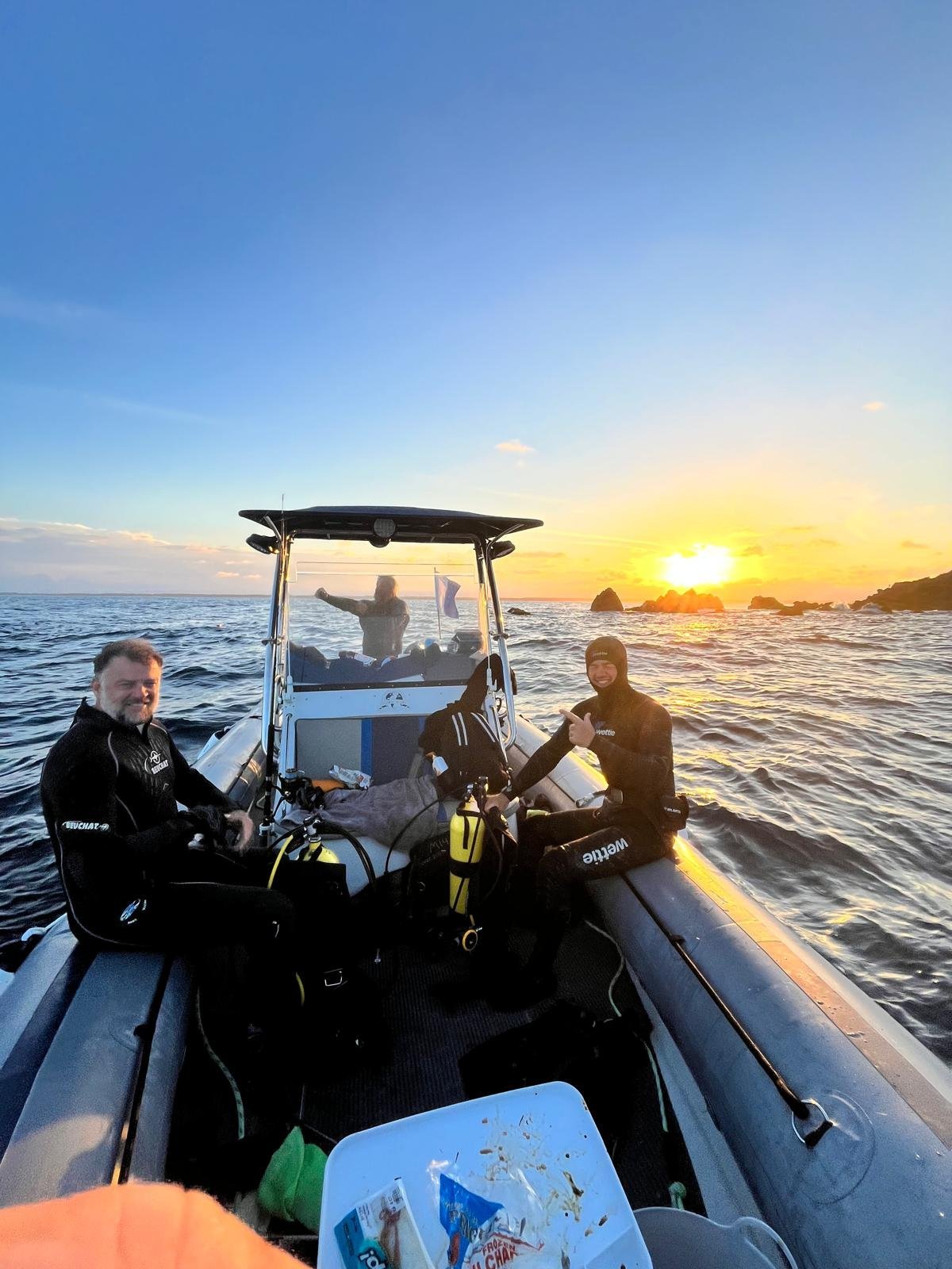 Scuba divers in wetsuits on a speedboat at sunset with other boats visible on the water