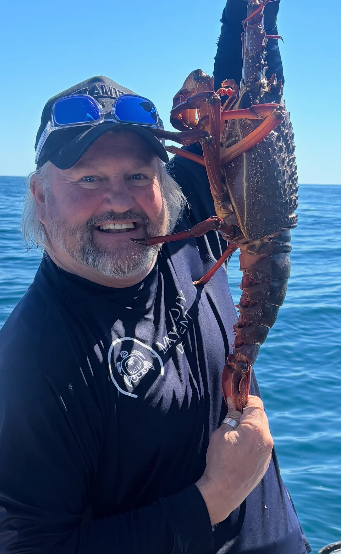 Smiling scuba diver in wetsuit holding a large caught crustacean over blue ocean water