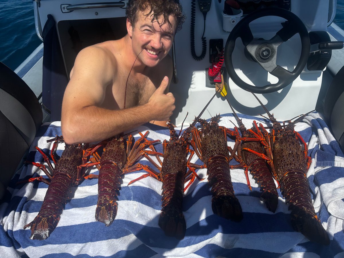 Man on boat giving thumbs up next to row of caught lobsters on striped towel