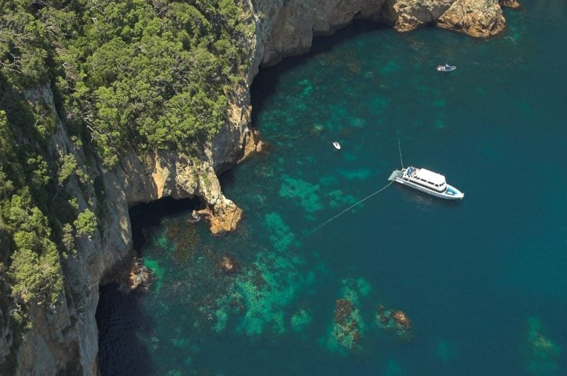 Aerial view of rocky coastal cliffs with turquoise water and two anchored boats below